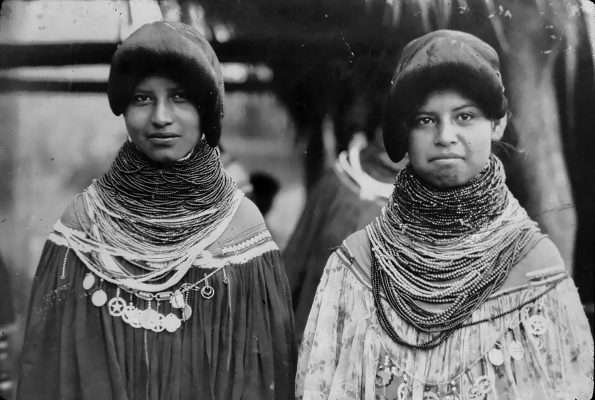 Historic black-and-white photograph of two Seminole women wearing traditional clothing and layered bead necklaces.