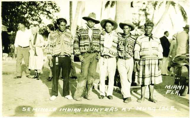 Historic photograph of five Seminole men at Musa Isle in Miami, Florida, wearing patterned clothing.